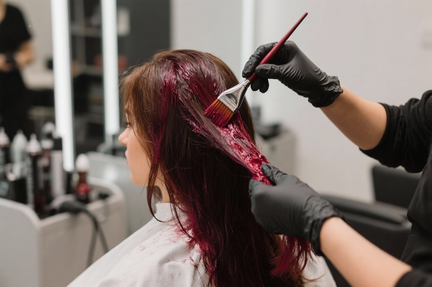 Coiffeur professionnel appliquant une coloration cherry cola sur cheveux bruns en salon moderne